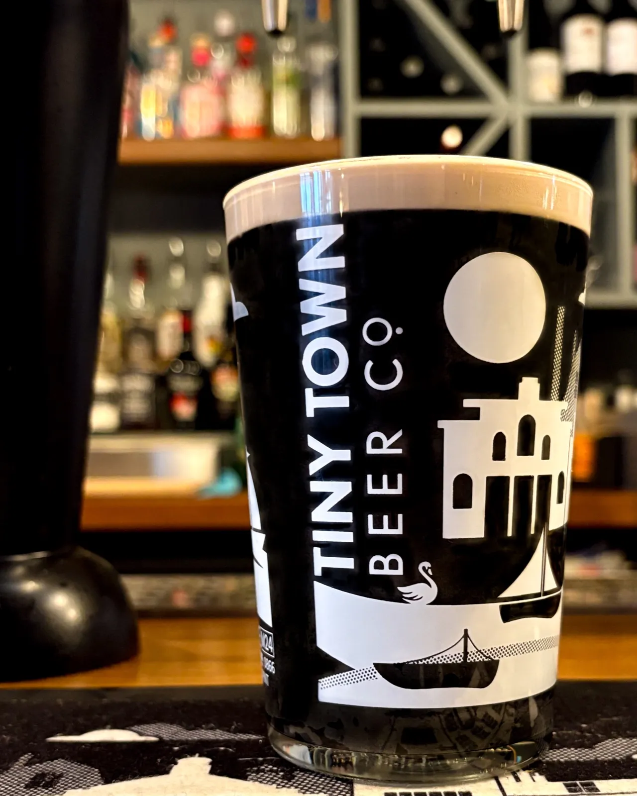 A pint of Black Swan stout in a Tiny Town glass on a pub bar